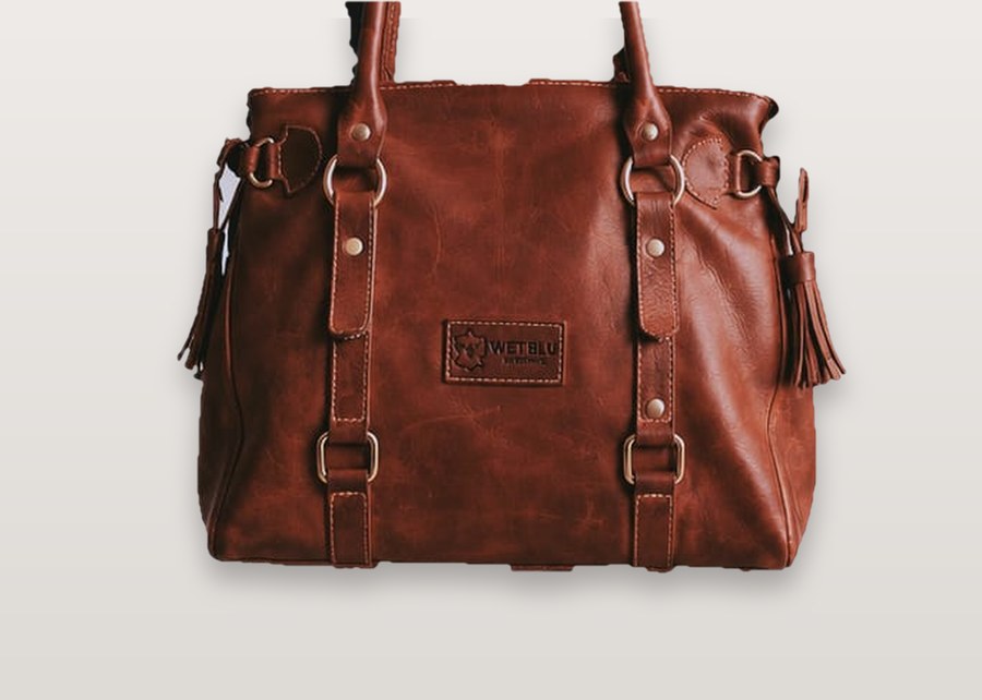 Tan leather tote with brass rivets, tassels and WetBlu logo plate